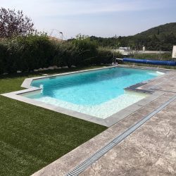 Vue d'ensemble de la plage de piscine, moitié béton imprimé motif roche gris, moitié gazon artificiel.