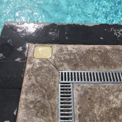 Zoom sur le caniveau et le coffrage du regard rehaussé du point électrique du projecteur de piscine. La plage en béton imprimé est à fleur de margelle, à la demande du client.